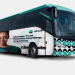 VooPay bus wrap design featuring a smiling woman using a smartphone, teal and black circular patterns, and the tagline ‘Manage your finances anytime, anywhere.