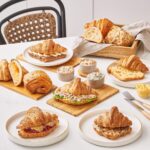 An assortment of freshly baked croissants and pastries served with spreads on a white table, showcasing buttery layers, fillings, and a cozy café setup.